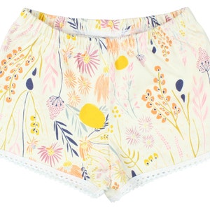 May include: White cotton shorts with a floral print in shades of pink, yellow, orange, and blue. The shorts have a white lace trim around the hem.