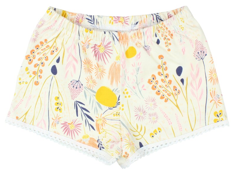 May include: White cotton shorts with a floral print in shades of pink, yellow, orange, and blue. The shorts have a white lace trim around the hem.