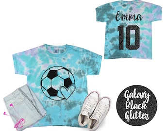 May include: A blue tie-dye t-shirt with a black soccer ball and heart design. The back of the shirt has the name "Emma" and the number "10" in black glitter.