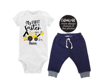 Puede incluir: Un body blanco con un gráfico de vehículo de construcción amarillo y el texto "My First Easter 2025 Owen". Un pantalón de chándal azul marino con un cordón blanco.