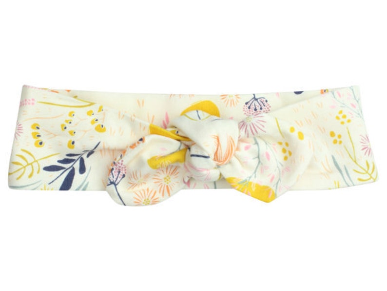 May include: A white headband with a floral pattern in shades of yellow, pink, and blue. The headband is tied in a knot at the top.