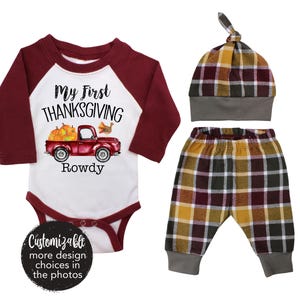 Könnte beinhalten: Ein Baby-Outfit-Set mit einem rot-weißen Strampler, auf dem "My First Thanksgiving" mit einem roten Lastwagen und Kürbissen steht, einer Hose aus burgunderrotem und gelbem Karomuster und einer burgunderroten und gelben Karomütze.