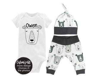 Könnte beinhalten: Ein weißer Baby-Strampler mit dem Namen "Owen" und einer Schwarz-Weiß-Bärenillustration. Ein passender Hut und eine Hose mit Weiß-Grau-Bärenmuster sind ebenfalls enthalten.