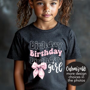 May include: A dark gray t-shirt with the text "Birthday Birthday Birthday girl" in white and pink. A pink bow is centered on the shirt. The text "Customizable more design choices in the photos" is in white on a black circle.