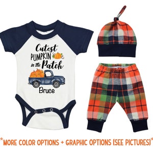 May include: A baby outfit set with a white bodysuit with a blue and white baseball style sleeve, a blue and white plaid hat, and blue and white plaid pants. The bodysuit has a graphic of a blue truck with pumpkins and the text "Cutest Pumpkin in the Patch" and "Bruce".