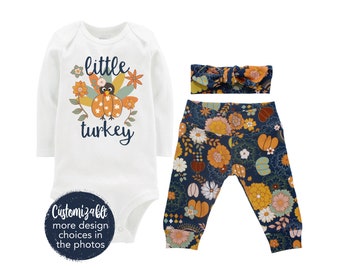 May include: A white long-sleeved bodysuit with the text "little turkey" and a cartoon turkey with autumn-coloured feathers. The bodysuit is paired with blue leggings with a floral pattern in orange, yellow, and white. A matching headband with a bow is also included.