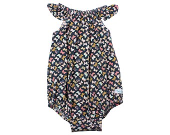 Puede incluir: Un pelele de bebé azul oscuro con estampado de mariposas. El pelele tiene mangas con volantes y un escote fruncido. El pelele tiene una pequeña etiqueta blanca con el texto "Two Peas" en la parte inferior derecha.
