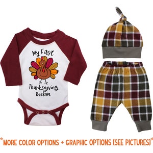 May include: A baby outfit set with a white bodysuit with a maroon raglan sleeve, a turkey graphic, and the text "My First Thanksgiving Beckham". The set also includes a pair of plaid pants and a matching plaid hat.