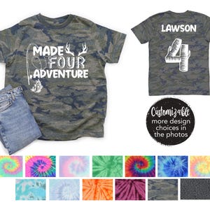 May include: A camouflage-patterned t-shirt with the text "MADE FOUR ADVENTURE" in white, along with a fishing rod and deer antlers graphic. A pair of blue jeans is next to the shirt. The back of the shirt has the name "LAWSON" and the number "4".