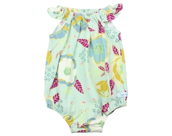 May include: A light blue baby onesie with a floral print featuring yellow, pink, and blue flowers. The onesie has ruffled sleeves and a gathered neckline. The text "Two Drops" is visible on the bottom right corner of the onesie.