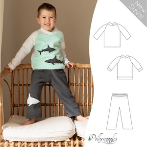 Pode incluir: Um padrão de roupa para crianças que inclui uma camisa de manga comprida e calças com um design de tubarão. A camisa é branca com um painel verde menta e as calças são cinzas com um tubarão branco na perna. O padrão está disponível em novos tamanhos. "Pollywoggles" é o nome da empresa de padrões.