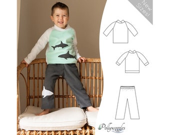 May include: A child's clothing pattern for a long-sleeved shirt and pants with a shark design. The shirt is white with a mint green panel and the pants are gray with a white shark on the leg. The pattern is available in new sizes. "Pollywoggles" is the name of the pattern company.