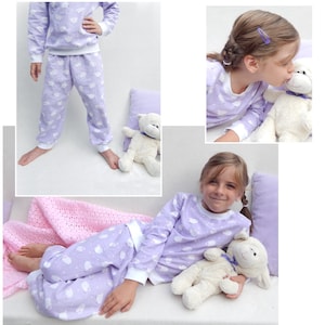 May include: A girl wearing a lavender pajama set with a white sheep print. She is holding a white plush toy sheep. The pajamas have long sleeves and long pants. The girl is smiling and looking at the camera.