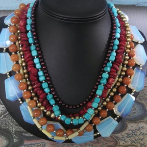 Op de afbeelding: Meerstrengige ketting met turquoise, rode koraal en opaal kralen. De ketting is gelaagd met verschillende kleuren en texturen, wat een bohemian stijl creëert.