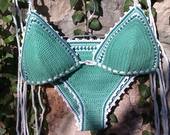 Puede incluir: Un bikini de crochet verde con ribetes y lazos blancos. La parte superior del bikini tiene forma triangular y la parte inferior es de talle alto.