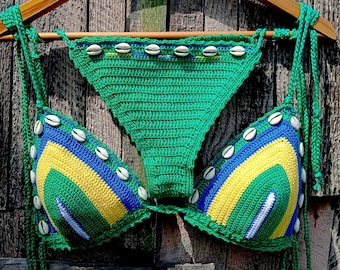 May include: Green, yellow, and blue crocheted bikini top and bottom with white shell accents. The bikini is hanging on a wooden hanger.