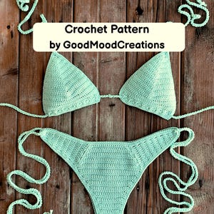Op de afbeelding: Een lichtgroene gehaakte bikiniset, bestaande uit een driehoekige top en een laag uitgesneden broekje, gepresenteerd op een houten oppervlak. De afbeelding bevat de tekst "Crochet Pattern by GoodMoodCreations". De bikini heeft strikjes.