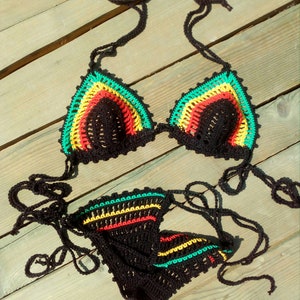 May include: A black crochet bikini top and bottom with green, yellow, and red stripes. The bikini is laid out on a wooden surface.