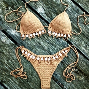 May include: A brown crocheted bikini with white shell accents. The bikini top and bottom have a fringe trim.
