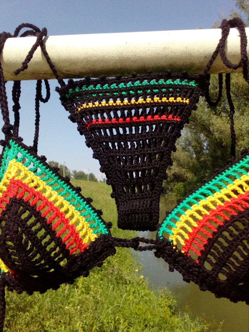 May include: A black crochet bikini top with green, yellow, and red stripes. The top is hanging on a white metal bar.