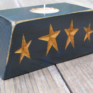 Może przedstawiać: Drewniany świecznik w ciemnoniebieskim kolorze z rzeźbionym wzorem gwiazdy. Świecznik ma małe, okrągłe wgłębienie na świecę.