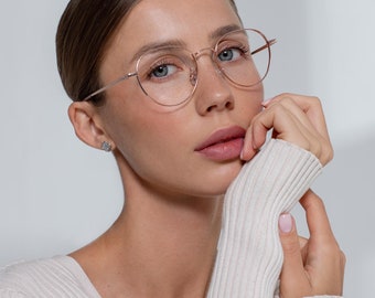 May include: A woman wearing rose gold round glasses with a white ribbed sweater.