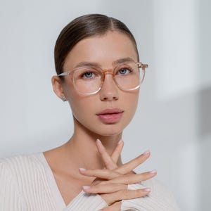 Könnte beinhalten: Runde, hellbraune Brille mit silbernen Bügeln. Die Brille wird von einer Person mit heller Haut, blauen Augen und hellbraunem Haar getragen. Die Person trägt einen cremefarbenen Pullover.