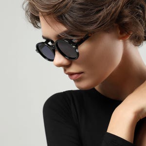 Side view of black round sunglasses with contrasting tortoiseshell temples worn by a woman.