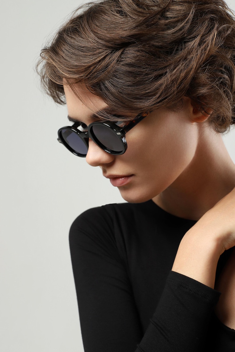 Side view of black round sunglasses with contrasting tortoiseshell temples worn by a woman.