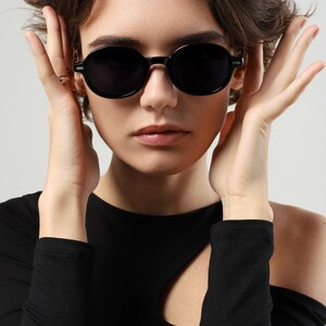 Woman wearing black round sunglasses, showing the rounded frame shape and dark polarized lenses from the front.