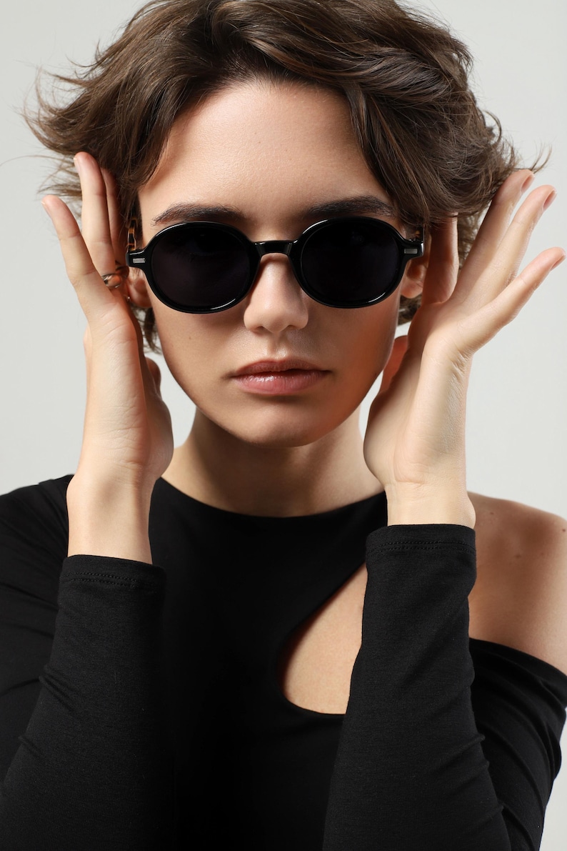 Woman wearing black round sunglasses, showing the rounded frame shape and dark polarized lenses from the front.