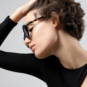 Woman wearing round black and tortoiseshell sunglasses, showing the frame shape and fit from the front.