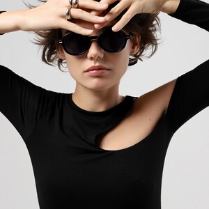Front-facing woman wearing round black sunglasses with dark polarized lenses and a glossy frame.