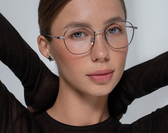 May include: A woman wearing silver-rimmed glasses with a black, sheer long-sleeved shirt.