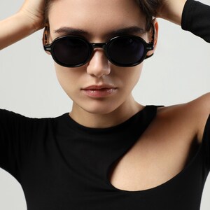 Woman shown from the side wearing black round sunglasses, highlighting the tortoiseshell temple design and frame fit.