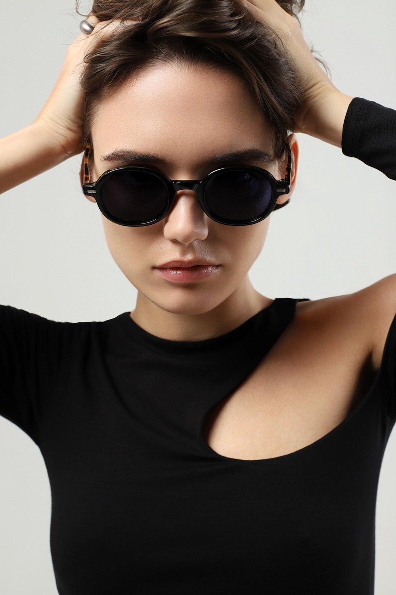 Woman shown from the side wearing black round sunglasses, highlighting the tortoiseshell temple design and frame fit.