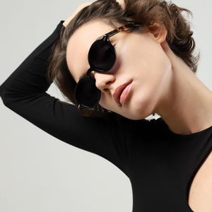 Front view of a woman wearing round black polarized sunglasses with dark lenses and contrasting tortoiseshell temples.