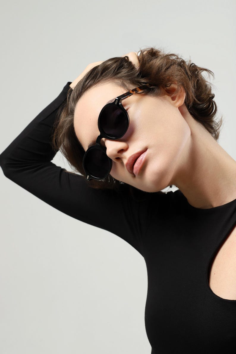 Front view of a woman wearing round black polarized sunglasses with dark lenses and contrasting tortoiseshell temples.