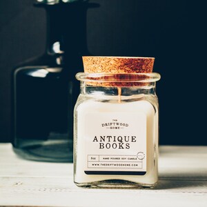 May include: A glass jar candle with a cork lid. The candle is labeled "The Driftwood Home" and "Antique Books". The candle is hand-poured soy and is 8 oz.