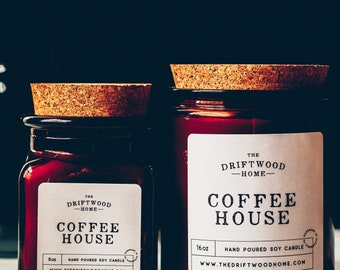 May include: Two red glass jars with cork lids. The jars have white labels that read "The Driftwood Home Coffee House" and indicate the candle is hand-poured soy. One jar is 8oz, the other is 16oz.