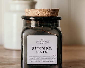 May include: A black glass jar with a cork lid and a white label that reads "The Driftwood Home - Summer Rain - 8oz Hand Poured Soy Candle - www.thedriftwoodhome.com"