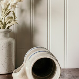 May include: A white ceramic mug with blue stripes around the top. The mug is turned upside down, showing the inside of the mug.
