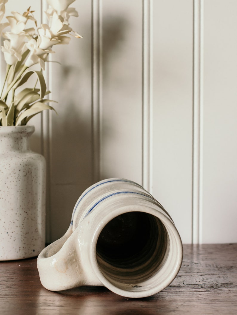 May include: A white ceramic mug with blue stripes around the top. The mug is turned upside down, showing the inside of the mug.