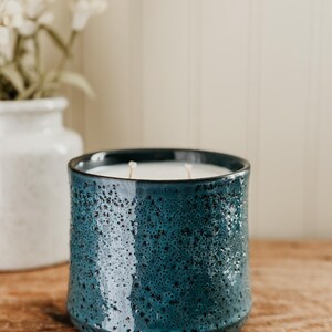 May include: A teal blue ceramic candle jar with a white wax candle inside. The jar has a textured surface.