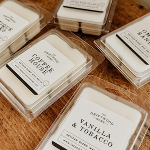 May include: A collection of wax melts in clear plastic containers with labels that read "The Driftwood Home". The scents include "Blue Ridge Cabin", "Coffee House", "Vanilla & Tobacco", "Ombre Sand", and "Tiki Sticks".