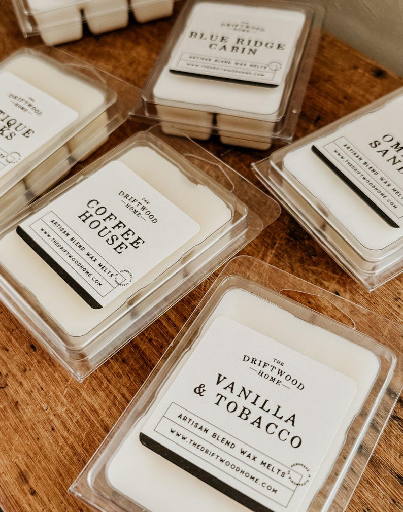 May include: A collection of wax melts in clear plastic containers with labels that read "The Driftwood Home". The scents include "Blue Ridge Cabin", "Coffee House", "Vanilla & Tobacco", "Ombre Sand", and "Tiki Sticks".