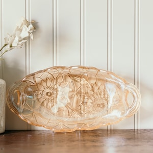 May include: A vintage glass serving dish with a floral design. The dish is made of clear glass with a frosted finish and features a raised floral pattern. The dish has two handles on the sides.