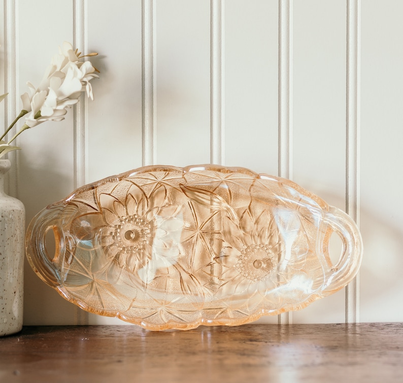 May include: A vintage glass serving dish with a floral design. The dish is made of clear glass with a frosted finish and features a raised floral pattern. The dish has two handles on the sides.
