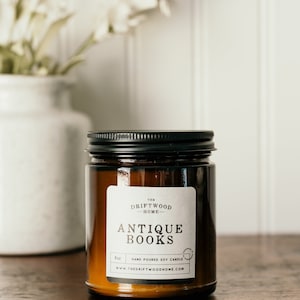May include: A brown glass candle jar with a black lid. The label reads "The Driftwood Home" and "Antique Books". The candle is hand-poured soy and is 8 oz.