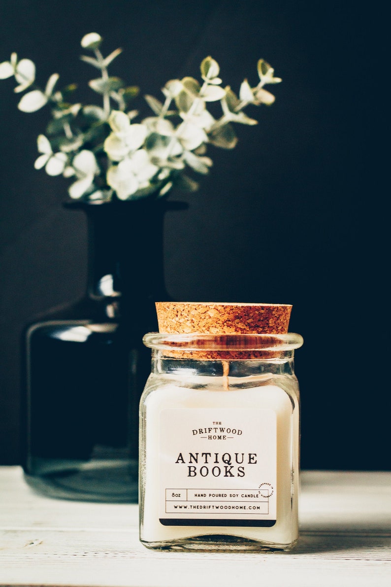 May include: A glass jar candle with a cork lid. The candle is labeled "The Driftwood Home" and "Antique Books". The candle is hand-poured soy and is 8 oz.